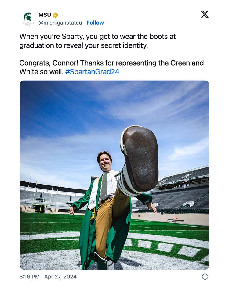 A tweet from Michigan State University that shows a student in a green graduate gown and the Sparty mascot boots on both of the student’s feet. One foot is lifted up toward the camera. The student is on the field of Spartan Stadium. There is accompanying text that reads: When you're Sparty, you get to wear the boots at graduation to reveal your secret identity. Congrats, Connor! Thanks for representing the Green and White so well. #SpartanGrad24