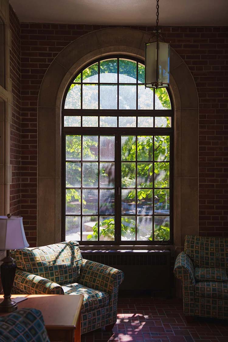 A gathering space that features a large window and light fixture and three chairs that have geometric upholstery.