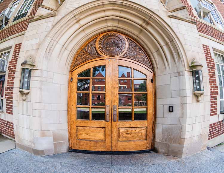 An ornate wooden carving at the top of a door that says Michigan State College of Agriculture and Applied Sciences founded 1855.