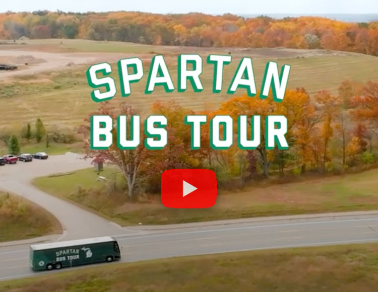 Fall trees and greenery with a road that has the green Spartan Bus Tour bus traveling through it.