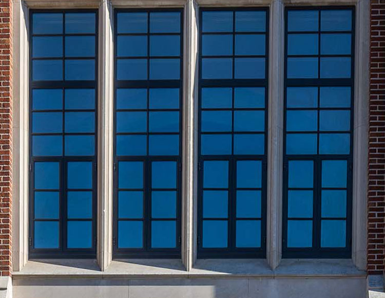 Four large windows that are between dark bricks on a building.